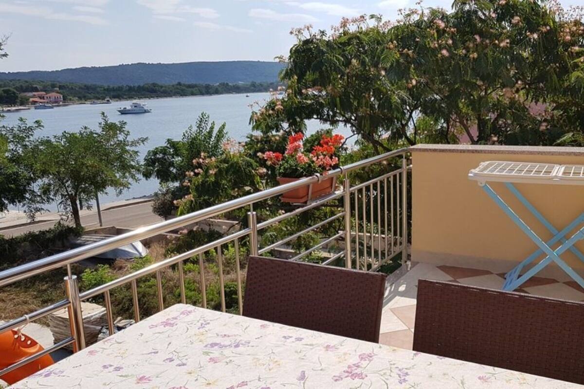 A balcony with a table and chairs, overlooking a body of water with boats and a distant shoreline.