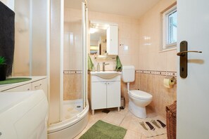 Une salle de bain avec une douche, des toilettes, un lavabo et une petite fenêtre.