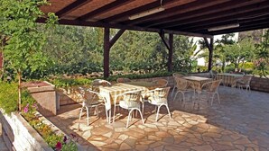 Un patio exterior con piso de piedra, mobiliario de ratán blanco y una estructura de pérgola.