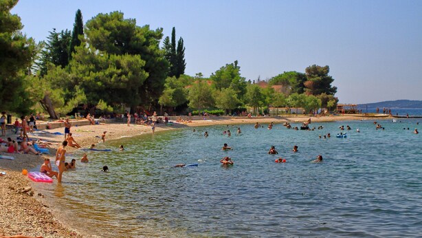 Une plage où l’on peut se baigner et bronzer, entourée d’arbres et sous un ciel dégagé.