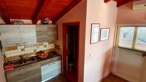 Une cuisine avec un mur recouvert de carreaux, des meubles en bois, un évier et une fenêtre avec des stores.