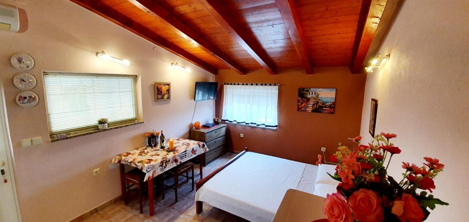 Una camera accogliente con travi in legno, un letto, una scrivania con una sedia, un tavolino con un vaso di fiori e una finestra con persiane.