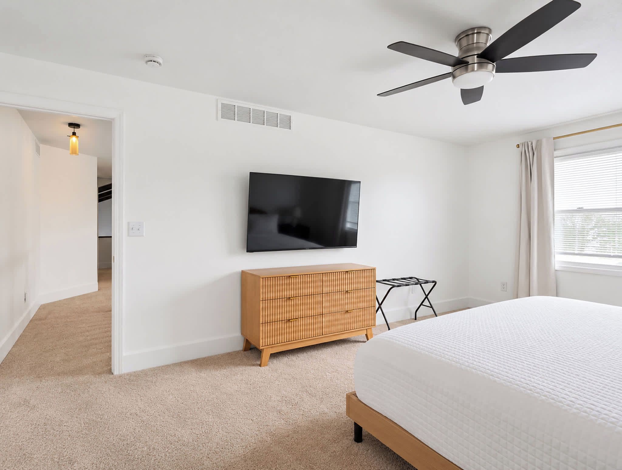 A bedroom with a bed, a television on the wall, a ceiling fan, and a wooden dresser.