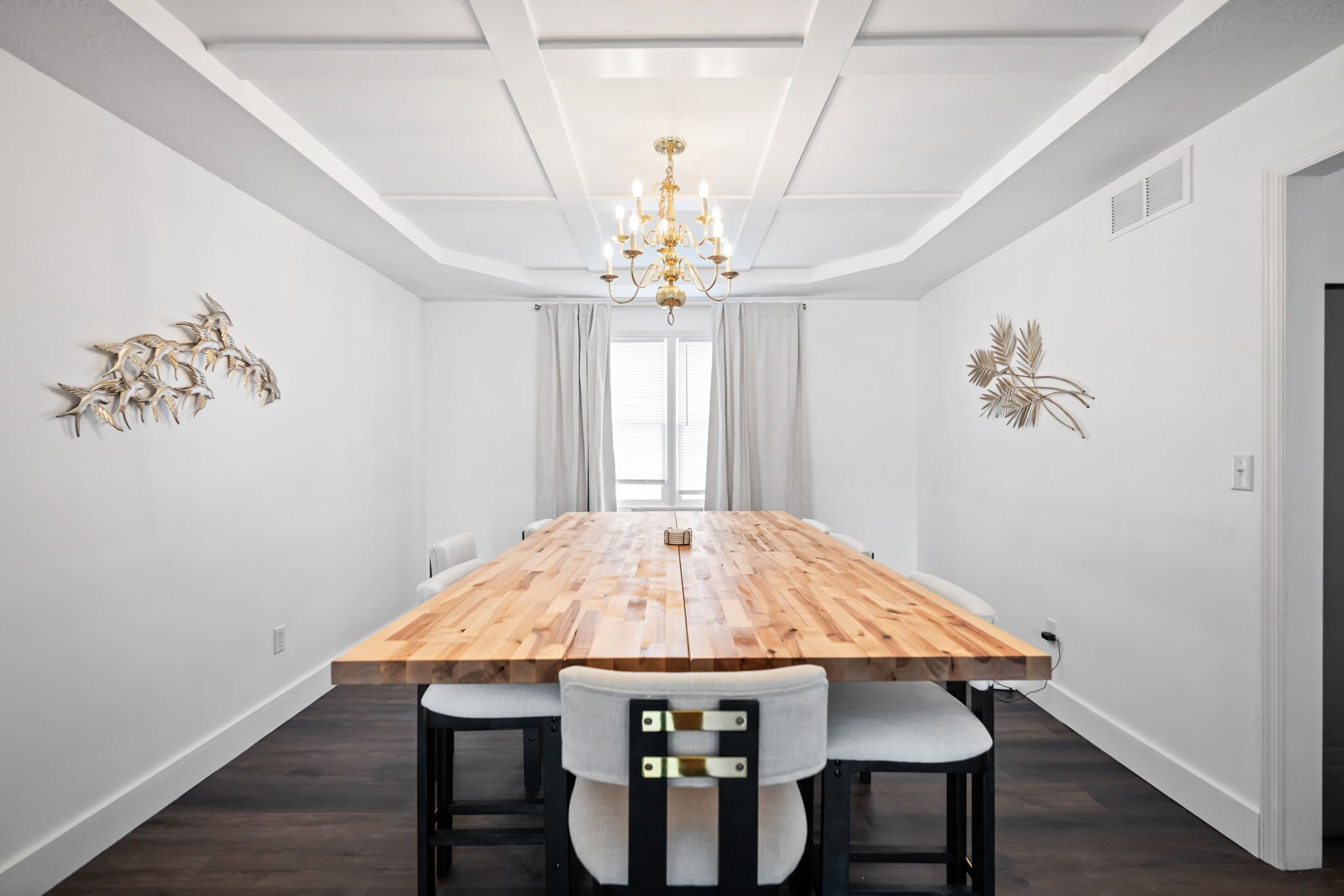 A modern dining room with a wooden table, white walls, and a chandelier.