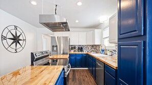 A modern kitchen with blue cabinets, stainless steel appliances, and a wooden countertop. - Nookside Grand Estate For 8 (Hamilton)
