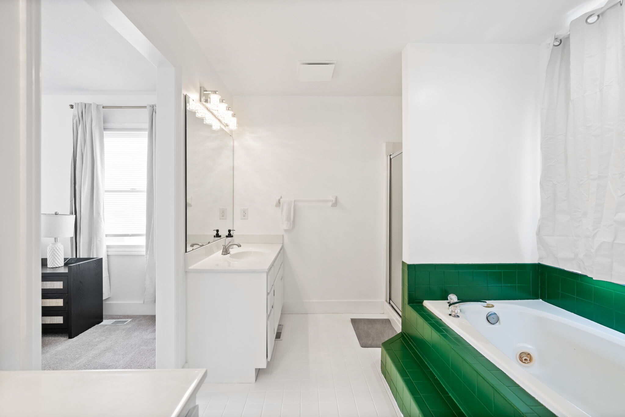 Une salle de bain moderne avec un lavabo blanc, une baignoire recouverte de carreaux verts et un grand miroir.