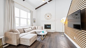A modern living room with a sectional sofa, a round coffee table, a fireplace, and a large window with curtains. - Nookside Grand Estate For 8 (Hamilton)