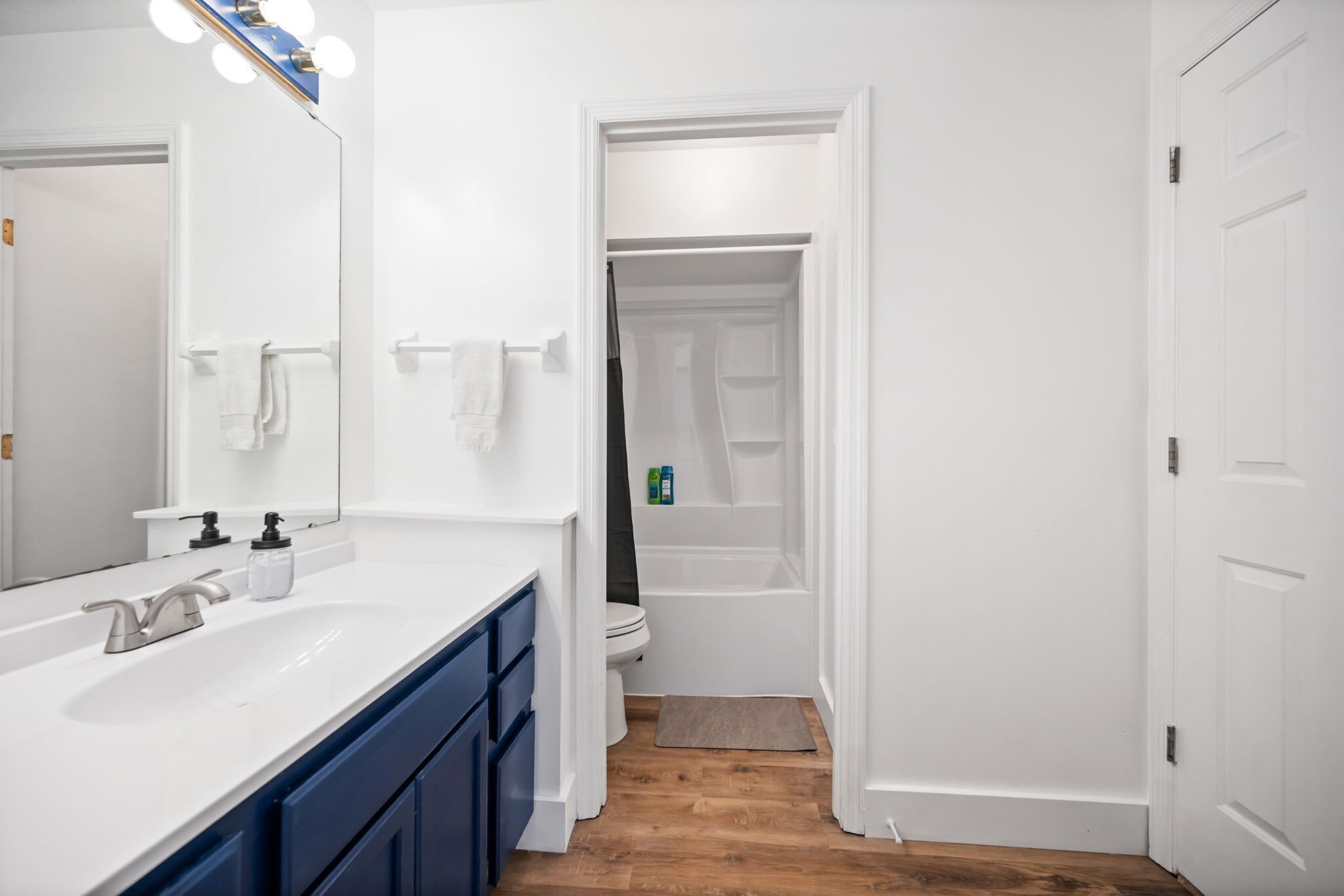 A modern bathroom with a white vanity, a mirror, and a shower area visible through an open door.