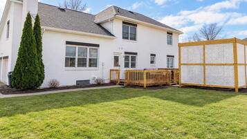 Une maison à deux étages, avec une façade blanche, un jardin clôturé et une terrasse en bois.