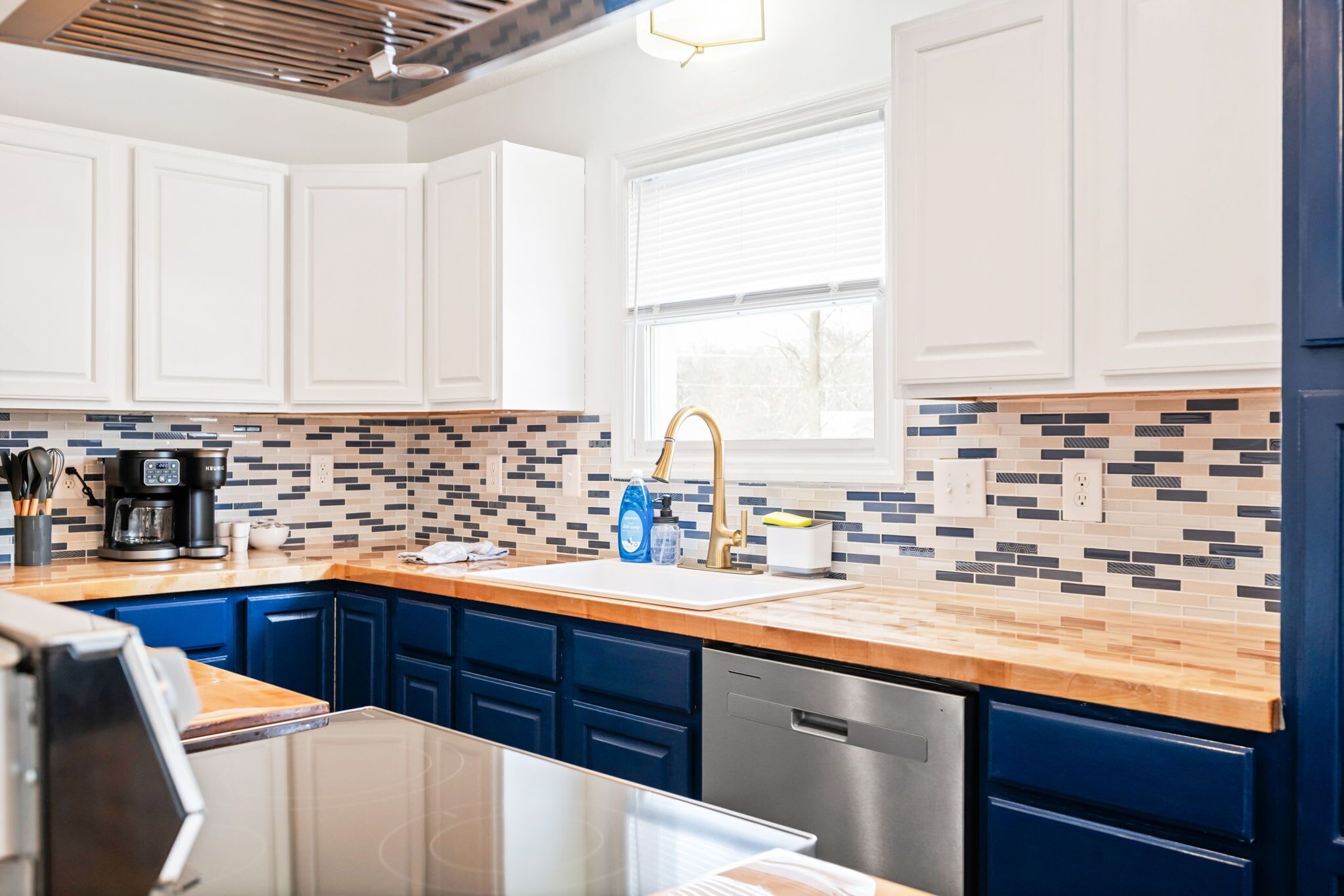 A modern kitchen with white cabinets, blue drawers, a wooden countertop, and a tiled backsplash.