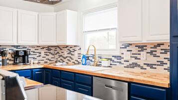 A modern kitchen with white cabinets, blue drawers, a wooden countertop, and a tiled backsplash.