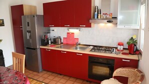 A compact kitchen with red cabinets, a stainless steel refrigerator, a gas stove, and a built-in oven. - Apartment Tomi (Hvar)