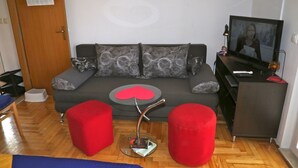 A modern living room with a grey sofa, two red ottomans, a glass coffee table, and a TV on a black stand. - Apartment Tomi (Hvar)