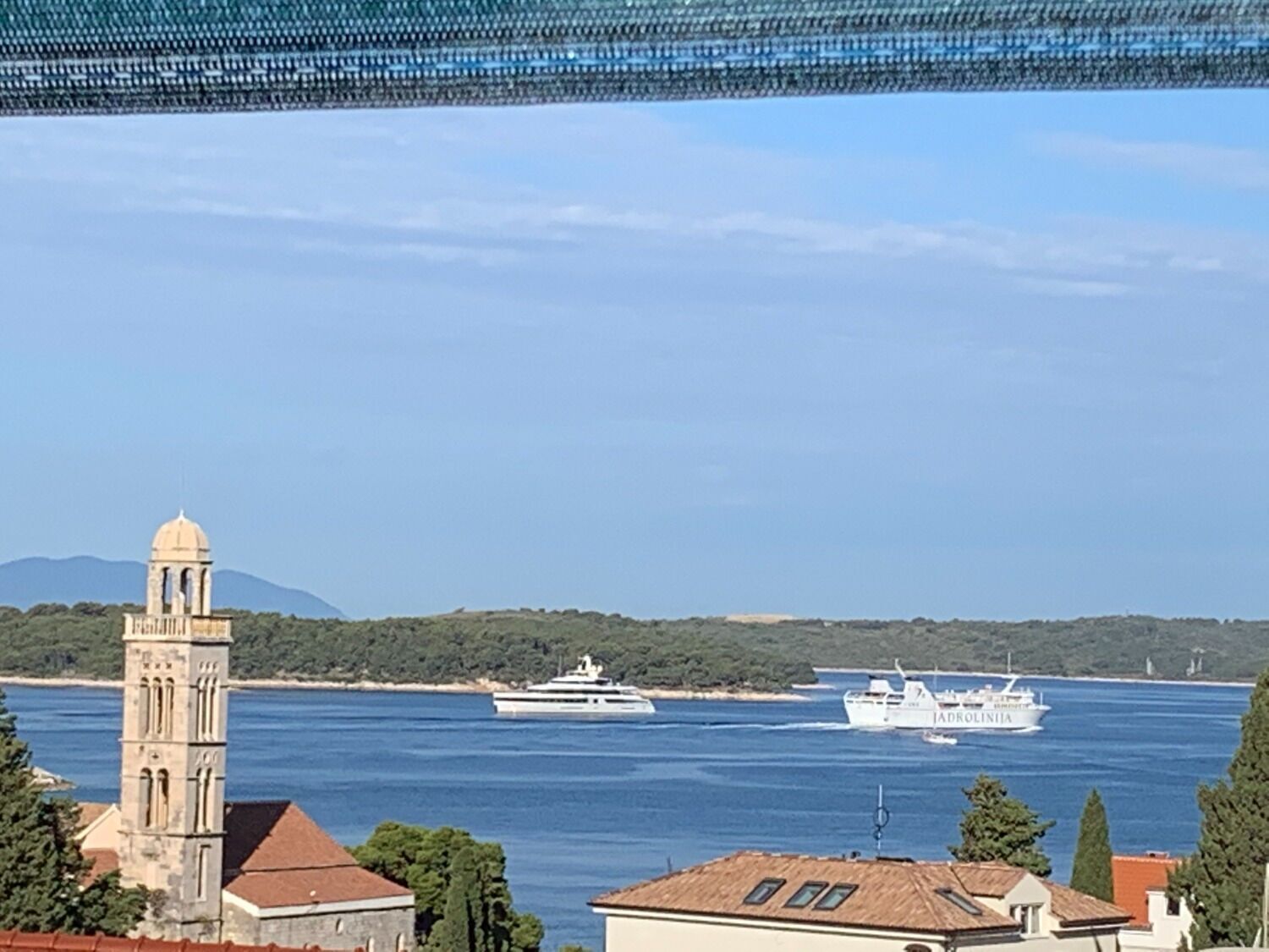 A coastal view with a church tower, a body of water, and a cruise ship named 'Adriatica' in the distance.