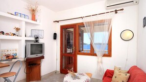 A compact living space with a television, a small table, a red sofa, and a window with a view. - Apartments Desa (Blato)