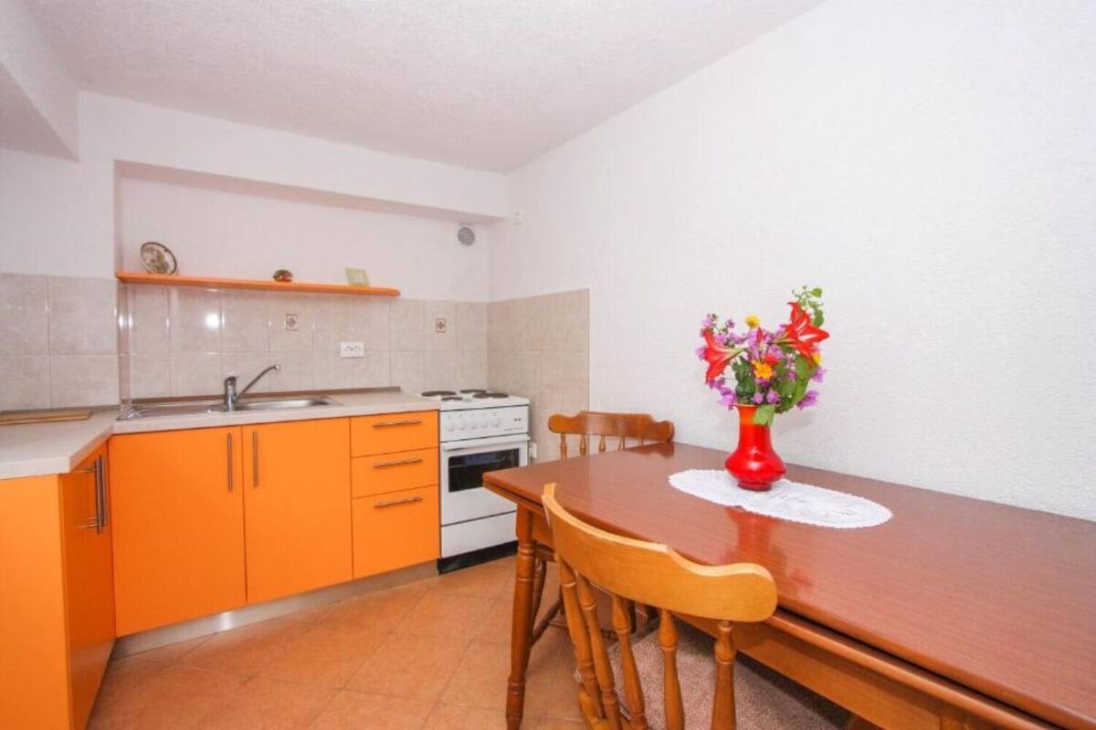 A compact kitchen with orange cabinets, a white stove, and a dining table with chairs.