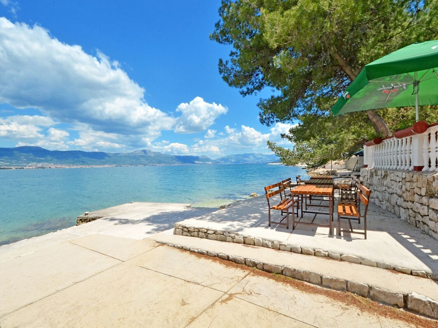 A seaside patio with a table and chairs, a stone wall, and a green umbrella.
