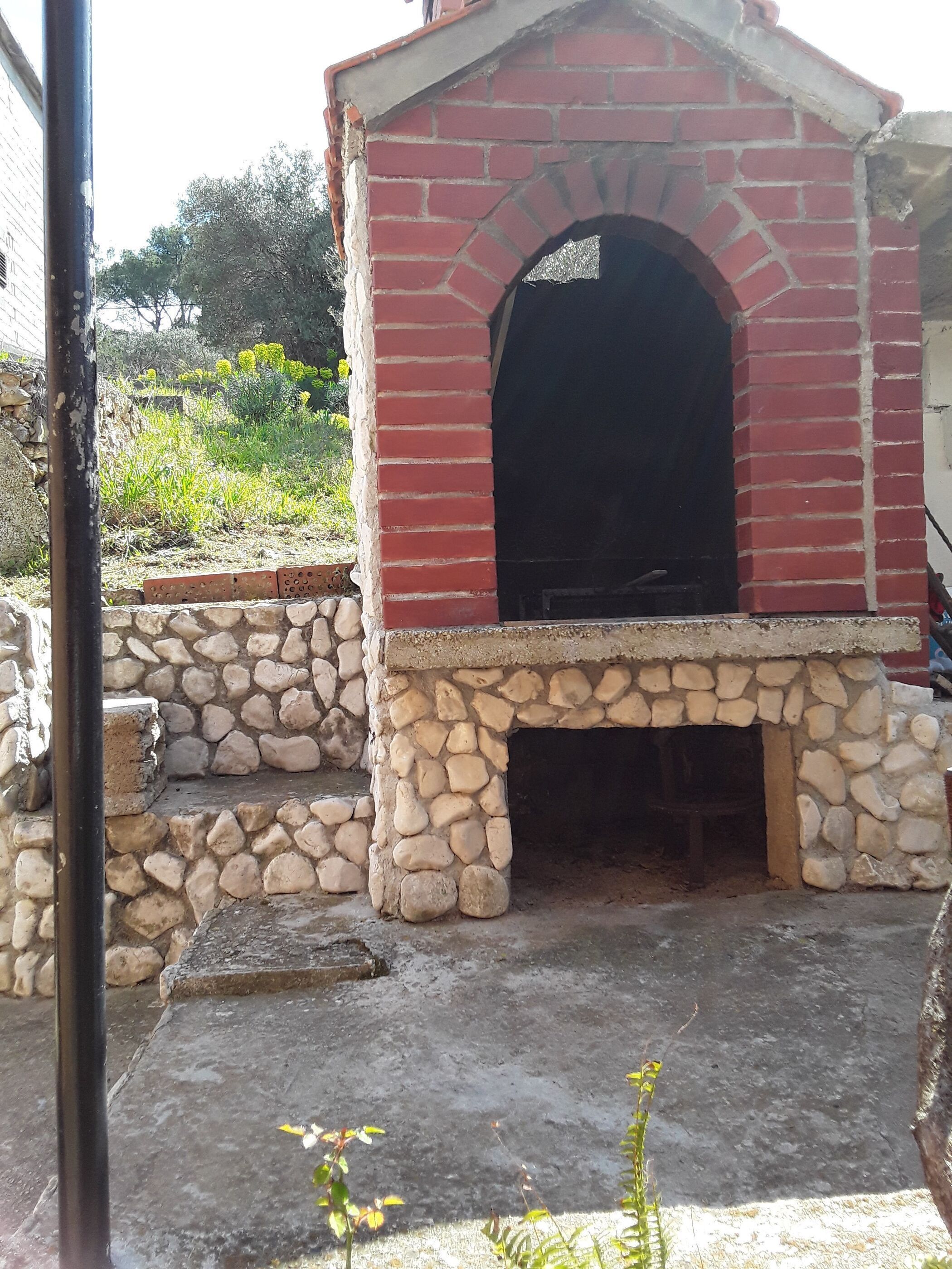 A stone-built outdoor structure with a brick chimney, surrounded by a stone wall and vegetation.