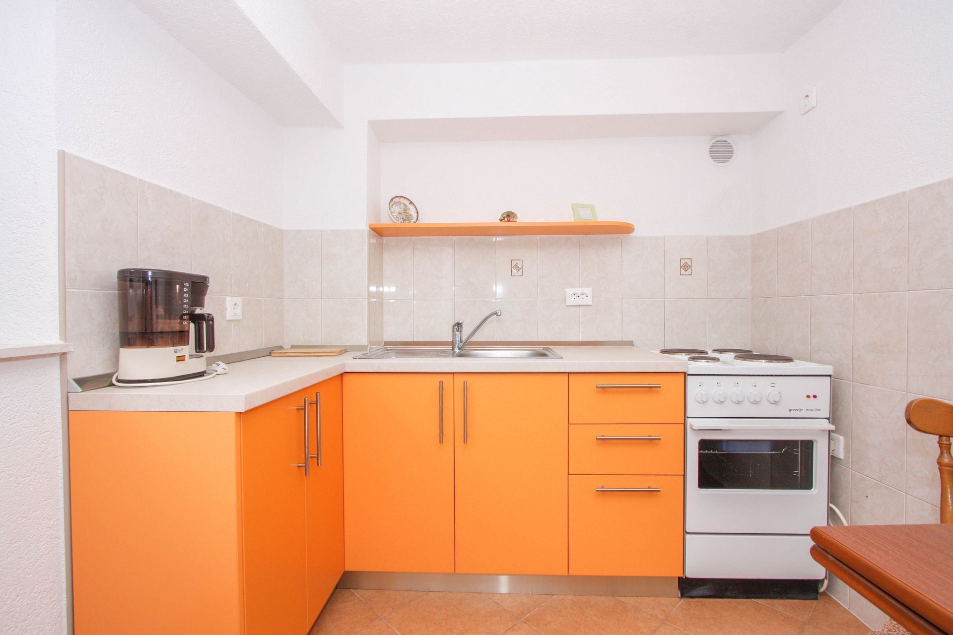 A compact kitchen with orange cabinets, a coffee maker, a sink, and a stove.