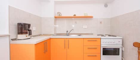 A compact kitchen with orange cabinets, a coffee maker, a sink, and a stove.