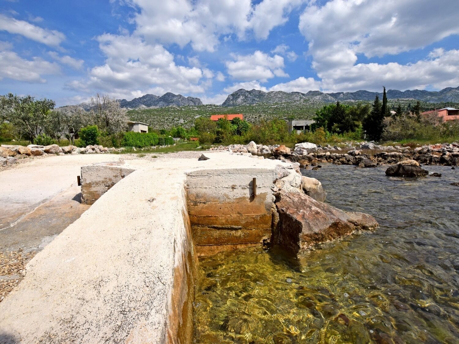 A clear outdoor pool area with a concrete structure, surrounded by rocks and a mountain backdrop.