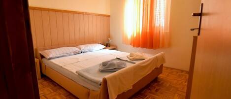 A bedroom with a wooden bed, a nightstand, and a window with orange curtains.