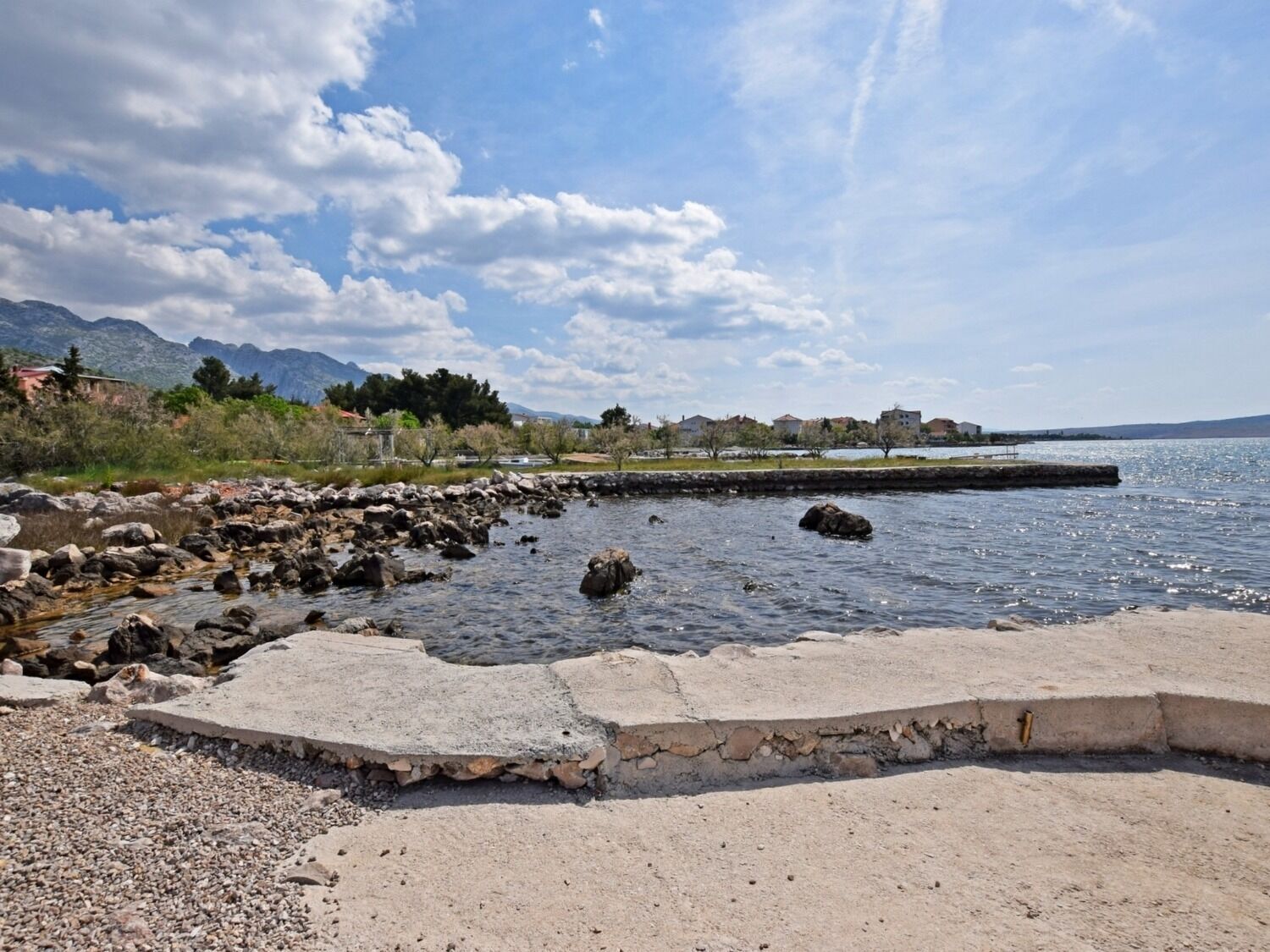 A rocky shoreline with a concrete walkway leading to a body of water.