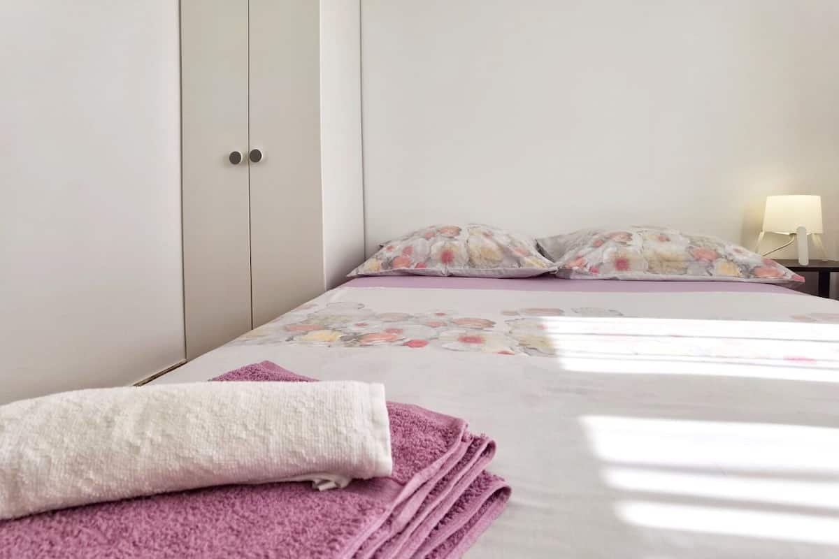 A neatly made bed with floral bedding, a white headboard, and a bedside table with a lamp.