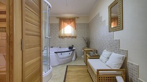 Un baño con bañera, ducha, inodoro y una pequeña zona de estar con cojín.