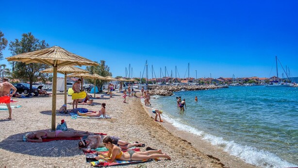 A beach with people sunbathing, umbrellas, and boats in the background. - House Andro (Bibinje)