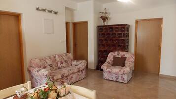 Una sala de estar con un sofá, un sillón, una mesa con un jarrón de flores y una estantería.