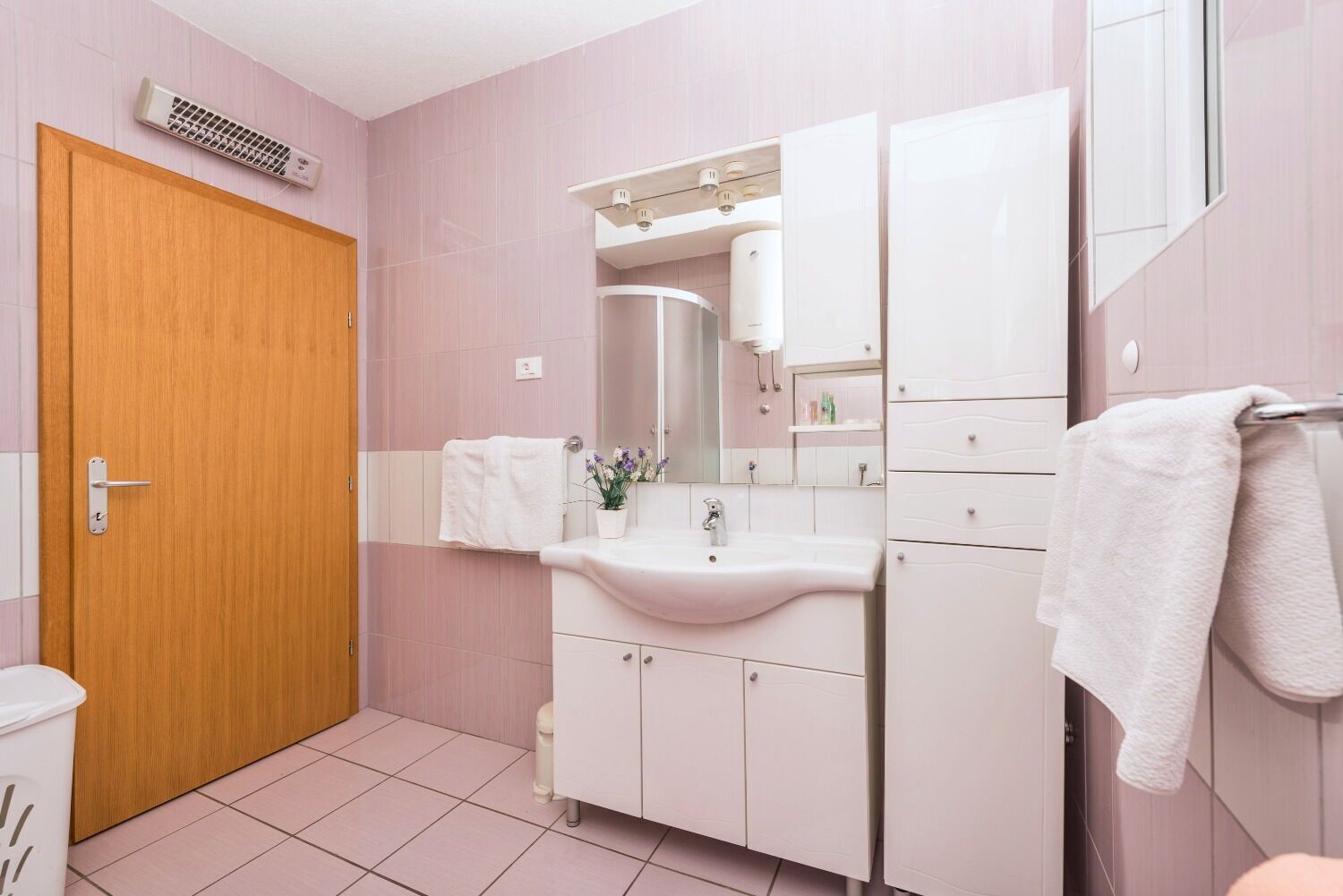A bathroom with a wooden door, white sink, and cabinets.