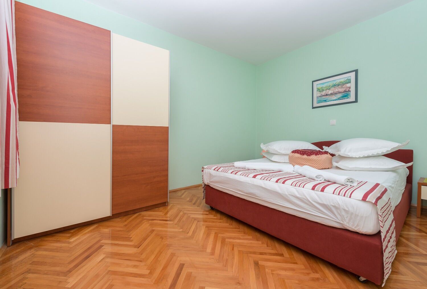 A bedroom with a bed, a wardrobe, and a painting on the wall.