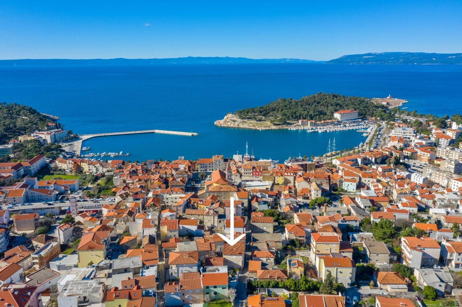 A coastal town with dense red-roofed buildings, a marina, and a prominent lighthouse.