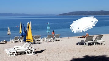 A beach with sun loungers and umbrellas, a clear view of the sea, and a distant hilly landscape.