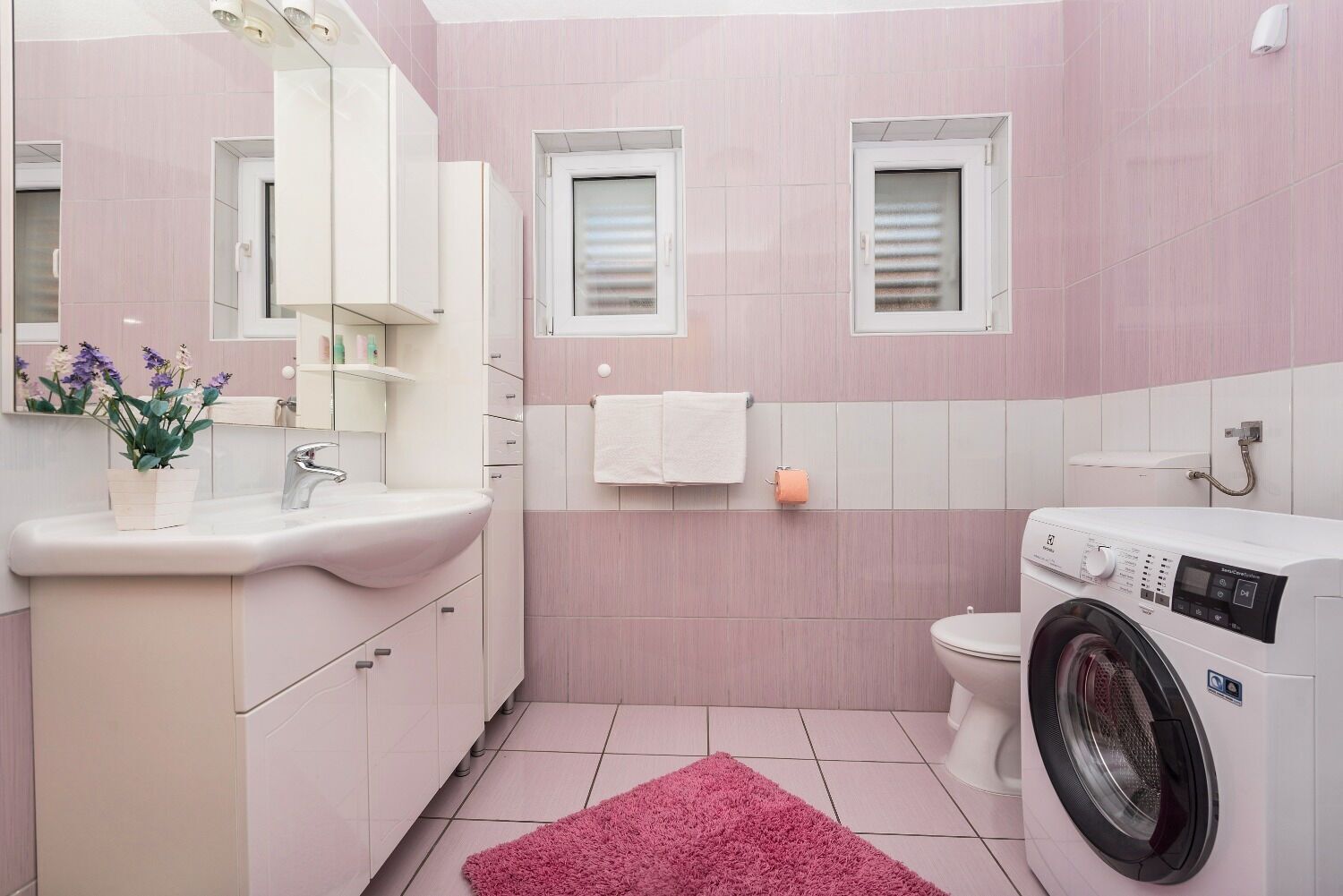 Ein Badezimmer mit Waschbecken, Spiegel, Handtuchhalter, Toilette und Waschmaschine.