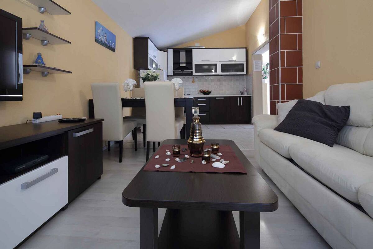 Un salon moderne avec un canapé, une table basse ornée d’un vase décoratif et un téléviseur posé sur un meuble.