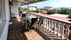 Un espace extérieur abrité, doté d’une table et de chaises, d’une rambarde et offrant une vue sur des maisons et des montagnes au loin.