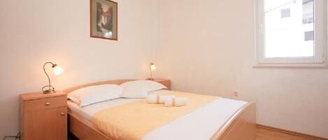 A neatly arranged bedroom with a bed, bedside tables, a framed picture, and a window.