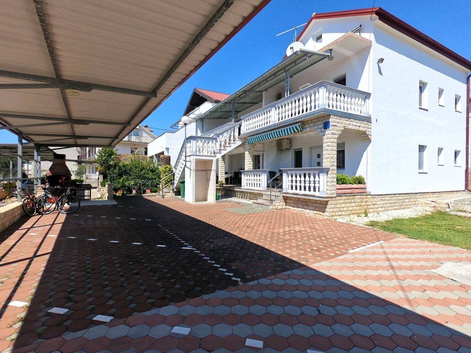 A covered outdoor area with a barbecue grill, a bicycle, and a white building with a balcony.