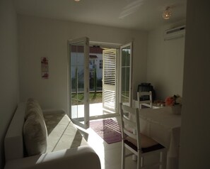 Ein Zimmer mit einem weißen Sofa, einem Esstisch mit einem Stuhl und einer Glastür zum Außenbereich.