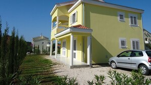 A two-story yellow building with a balcony, a car parked in front, and a well-maintained garden. - Apartments Mirjana (Pakostane)