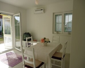 A dining area with a table set for two, white chairs, a vase with flowers, and a television on a stand. - Apartments Mirjana (Pakostane)