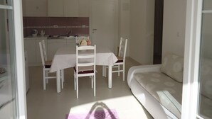A dining area with a table and chairs, a kitchen in the background, and a sofa in the foreground. - Apartments Mirjana (Pakostane)