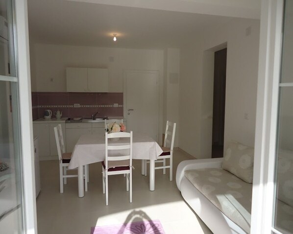 A dining area with a table and chairs, a kitchen in the background, and a sofa in the foreground. - Apartments Mirjana (Pakostane)