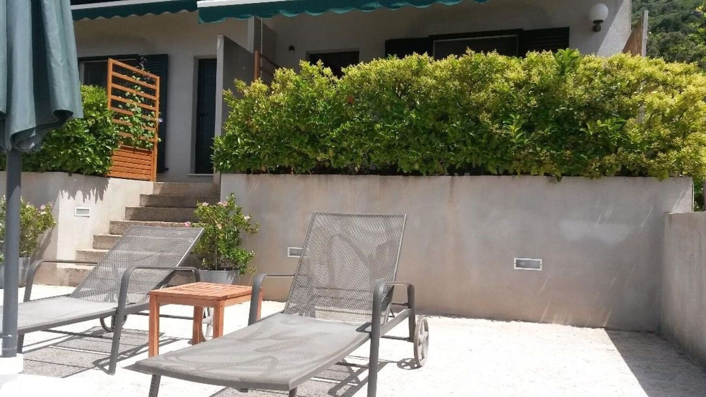 Un patio con dos sillones de descanso y una pequeña mesa, una escalera de madera y un muro de seto.