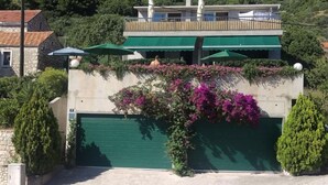 A two-story building with a green garage door, a balcony with green awnings, and a lush garden with purple flowers. - Apartments Horizont (Gradac)