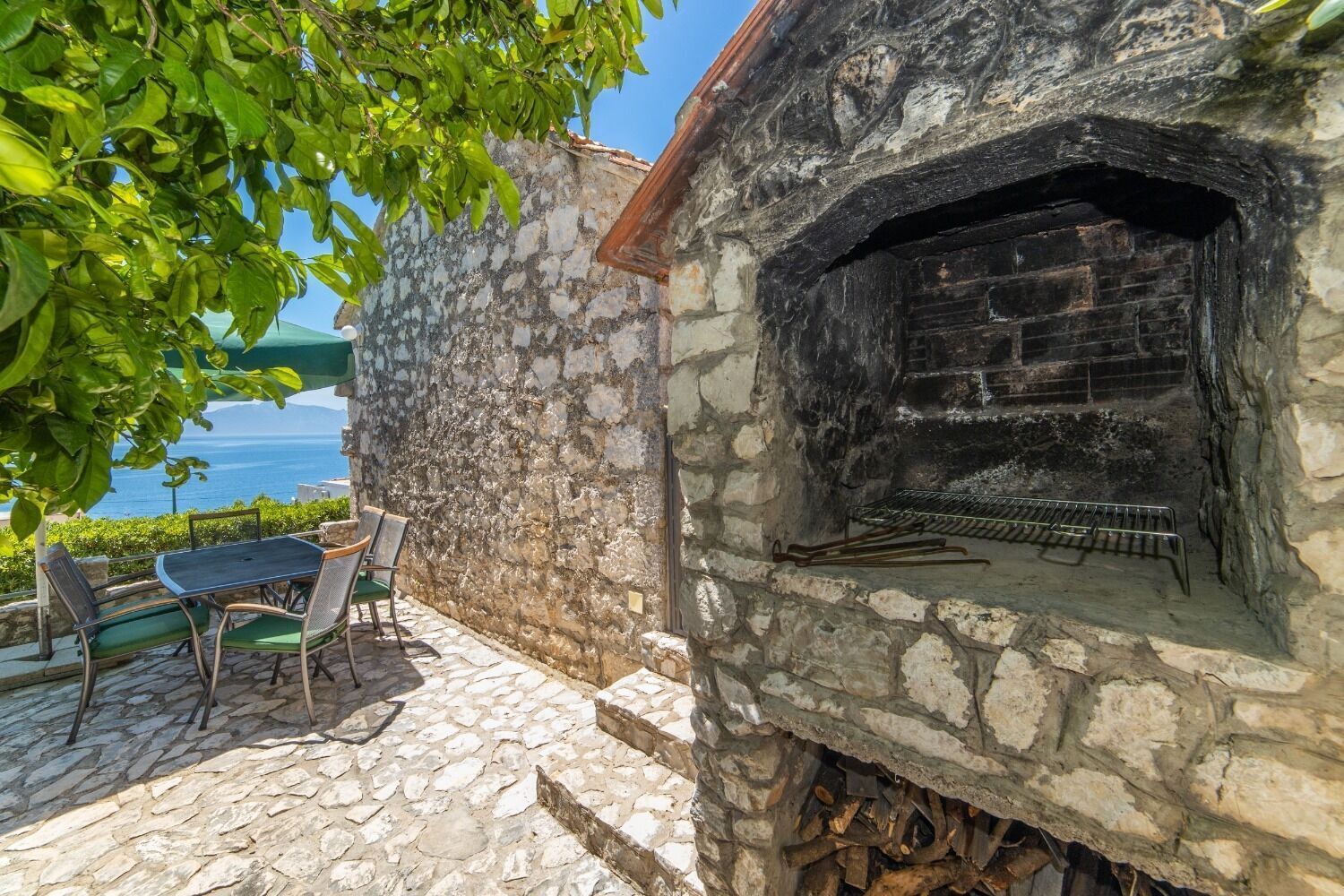 A stone building with a brick oven, a table with chairs, and a view of the sea.