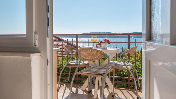 Un balcon avec une table et des chaises, un verre à la main et une vue sur la mer.