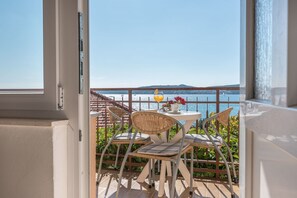 A balcony with a table and chairs, a glass of drink, and a view of the sea. - Apartments Vin (Seget)